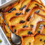 "A baked bread and butter pudding with golden, crisp top and custard-soaked layers in a white dish"
