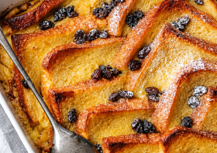 "A baked bread and butter pudding with golden, crisp top and custard-soaked layers in a white dish"