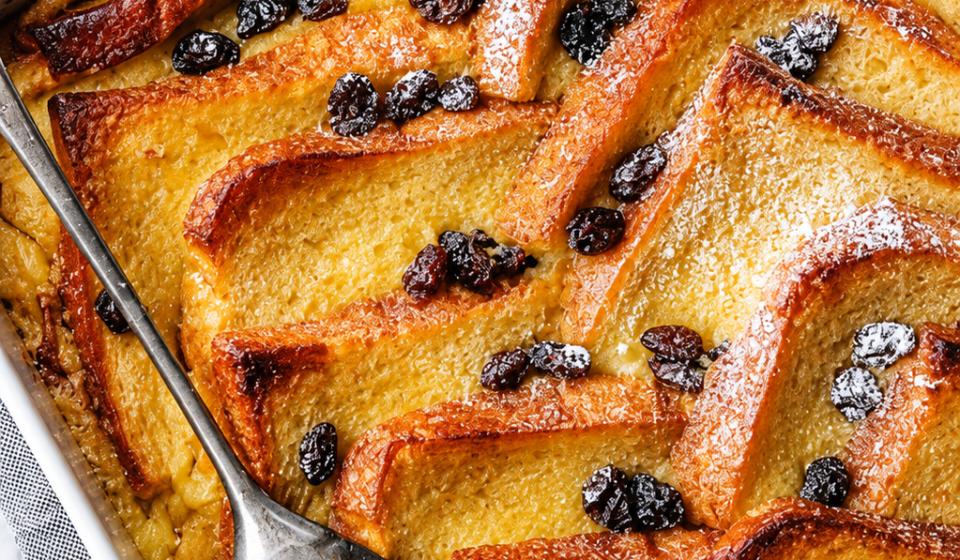 "A baked bread and butter pudding with golden, crisp top and custard-soaked layers in a white dish"
